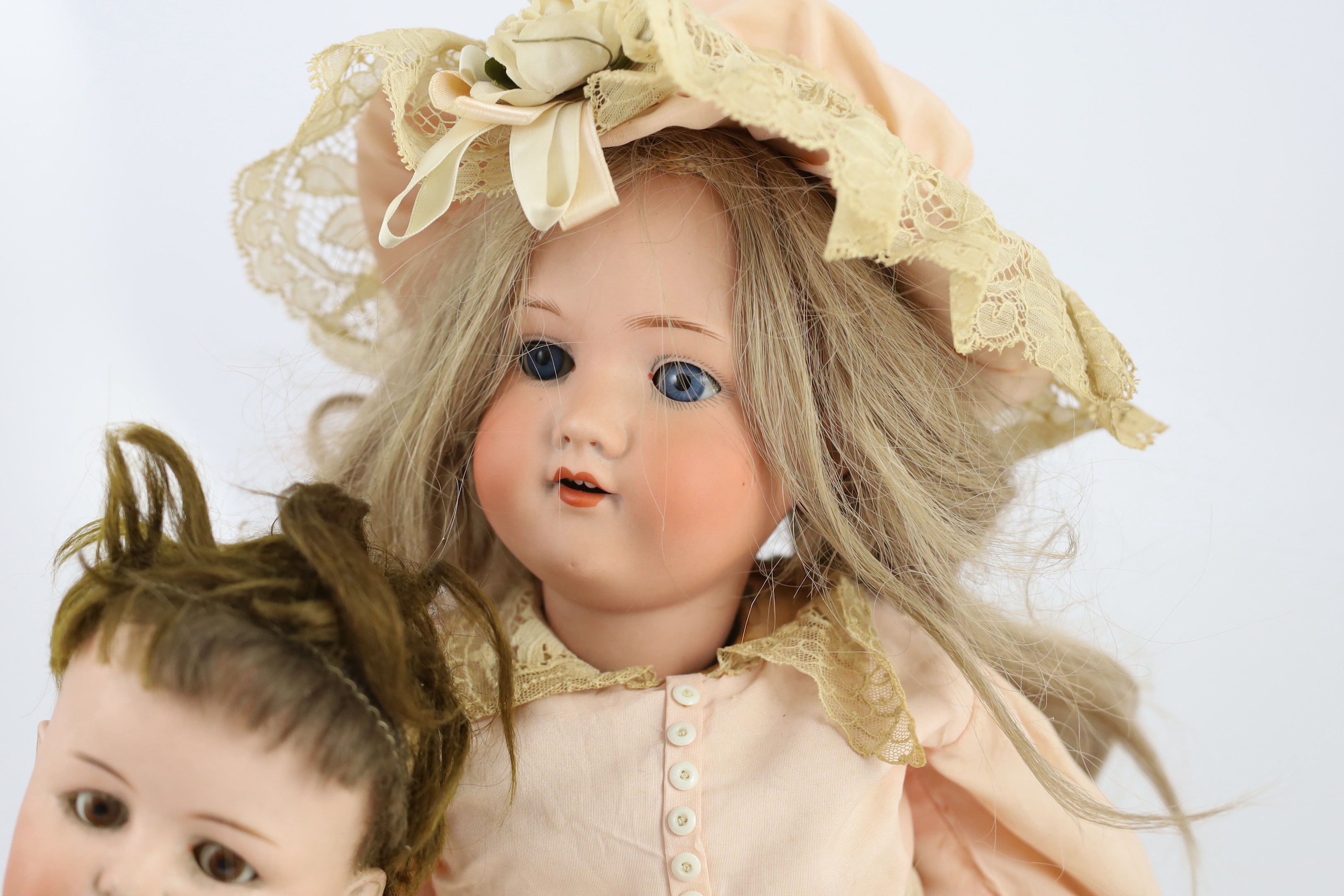 An Armand Marseille bisque doll, mould 390 with sleeping eyes and open mouth, jointed wood and composition body, cream and lace dress and matching bonnet, 22in., and a German Bebe Elite bisque doll